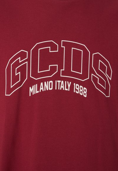 Červené bavlnené tričko s textúrovanou tkaninou, na prednej strane s bielym oblúkovým nápisom: "GCDS MILANO ITALY 1988".