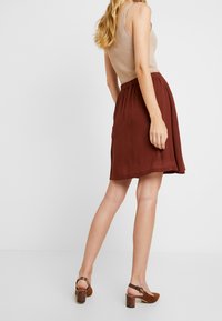 Brun veckad kjol gjord av lättviktig tyg, parat med en beige linne och bruna klacksandaler med en texturerad rem.