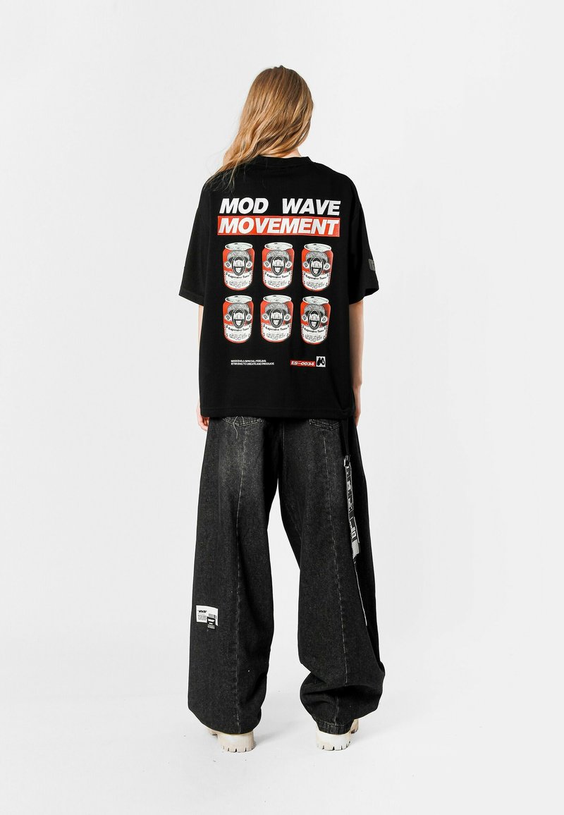 Camiseta negra de gran tamaño con gráficos en blanco y rojo en la parte de atrás, combinada con pantalones vaqueros de denim oscuro y holgados y zapatillas gruesas.