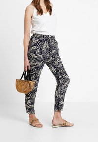 Navy kalhoty s bílým vzorem listů, elastickým pasem a zúženou nohavicí. Kombinované s bílým tílkem, hnědými sandály a kabelkou ve stylu bambusu.