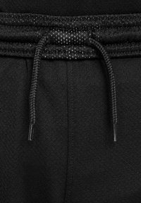 Pantalons de sport noirs avec une finition texturée, présentant un cordon de serrage avec des accents scintillants et des coutures renforcées à la taille.