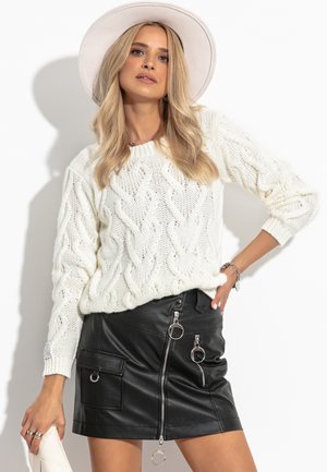 Sweter w dżersejowym splocie z białej przędzy, zestawiony z czarną spódnicą z sztucznej skóry z ozdobnym zamkiem błyskawicznym i metalowymi akcentami w kształcie pierścieni.