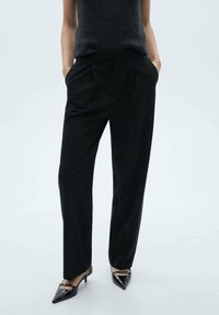 Black tailored trousers with a straight-leg fit, pleated front, and side pockets, complemented by pointed black heels.