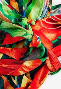 Färgglad tyg med ett blommönster i gröna, röda och gula nyanser, tvinnad i en knut med texturerade, lager-på-lager detaljer.