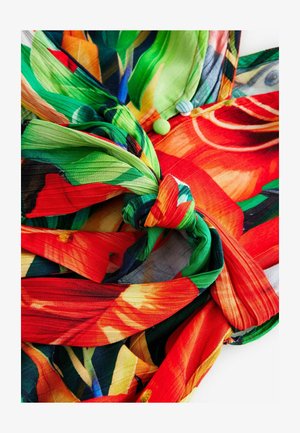 Farebná tkanina s kvetinovým vzorom v zelených, červených a žltých odtieňoch, zviazaná do uzla s textúrovanými, vrstvenými akcentmi.