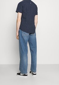 Námořnická krátká košile s bílým a růžovým geometrickým vzorem, doplněná volnými modrými džínami a černými teniskami.