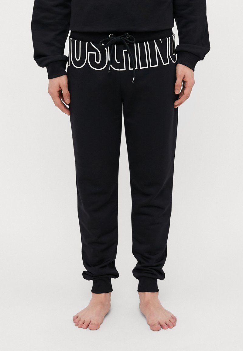 Black sweatpants with elastic waistband, drawstring detail, and contrasting white lettering on the front; tapered fit at the ankle.