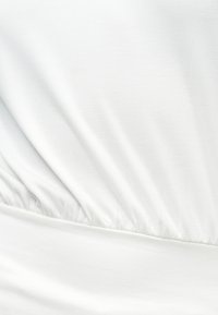 Κοντινό πλάνο λευκού υφάσματος με ραφή ελαστικού που δημιουργεί διακριτικές πτυχές και υφή.