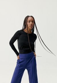 Top negro de manga larga con textura acanalada, combinado con pantalones azules de pierna ancha y cintura alta. El conjunto presenta una silueta ajustada y una textura suave.