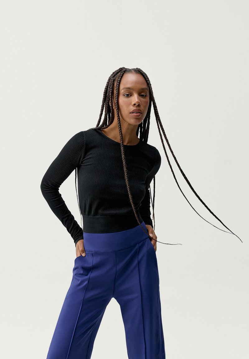 Top negro de manga larga con textura acanalada, combinado con pantalones azules de pierna ancha y cintura alta. El conjunto presenta una silueta ajustada y una textura suave.