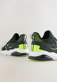 Black and neon green athletic shoes with a textured mesh upper, a chunky white midsole, and a contrasting black sole.