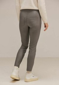 Grå, passande byxor med en slät textur, utrustade med två bakfickor, som bärs med vita sneakers och en krämfärgad tröja.