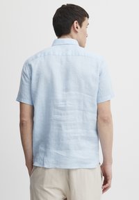 Camisa de manga corta azul claro de lino, con cuello y una textura suave, con dobladillo recto y mínimas arrugas.