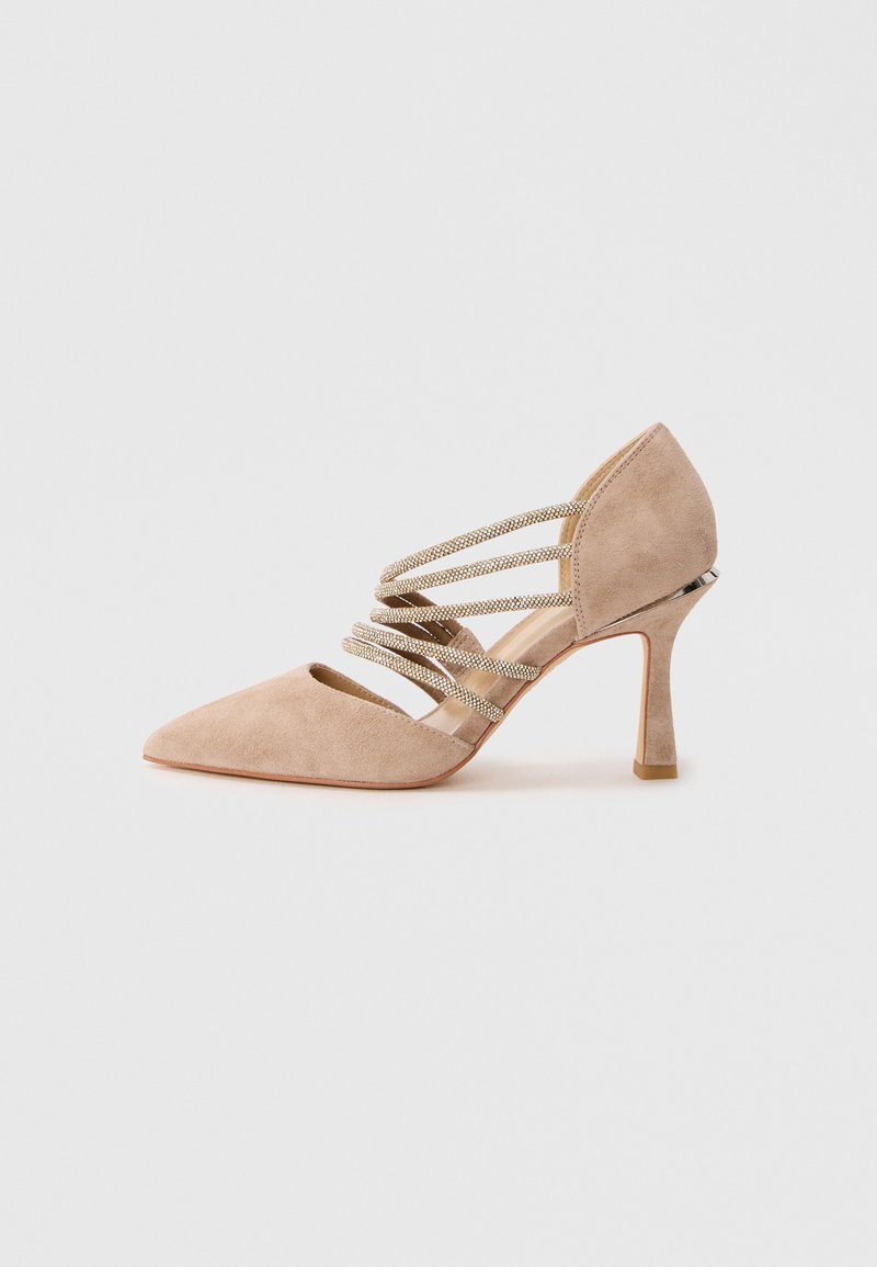 Chaussure à talon haut en suède beige, à bout pointu, avec des sangles décoratives métalliques et un talon fin de hauteur intermédiaire sur un fond blanc.