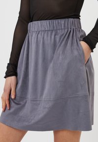 Gonna grigia con elastico in vita, realizzata in un morbido materiale simile alla pelle scamosciata, con due tasche laterali e una texture arricciata. Presenta dettagli di cuciture orizzontali.