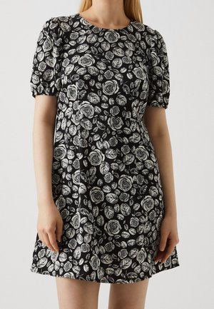 Svart klänning med vita blommiga ros- och bladmönster, korta puffärmar, rund halsringning och en flödande silhuett.