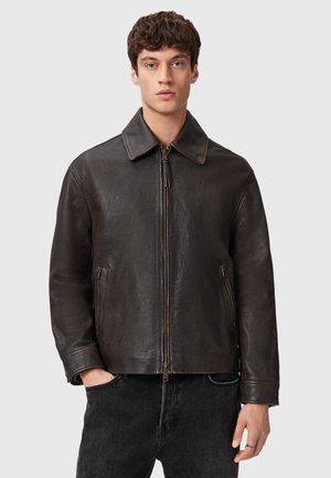 Braune Lederjacke mit spitzem Kragen und vorderem Reißverschluss, ausgestattet mit zwei seitlichen Taschen und einer strukturierten Oberfläche. Trägt man über schwarzen Jeans.