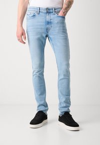 Jeans ajustados de color azul claro fabricados en denim, con un diseño de cinco bolsillos, un desvanecimiento sutil y cierre de cremallera; combinados con zapatillas negras.