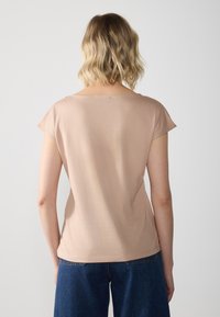 Kortærmet, lys beige top lavet af blød stof, med en rund halsudskæring og en afslappet pasform, sammen med mørkeblå brede bukser.