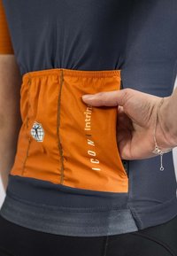 Haut de sport ajusté avec une partie supérieure bleue marine et une poche inférieure orange. Texte et logo sur la poche, avec un élastique froncé à la taille.