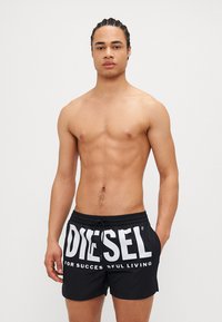Svarte svømmebukser med hvit "DIESEL"-logo og teksten "FOR SUCCESSFUL LIVING." Laget av lett materiale, med elastisk midjebånd og snøring.