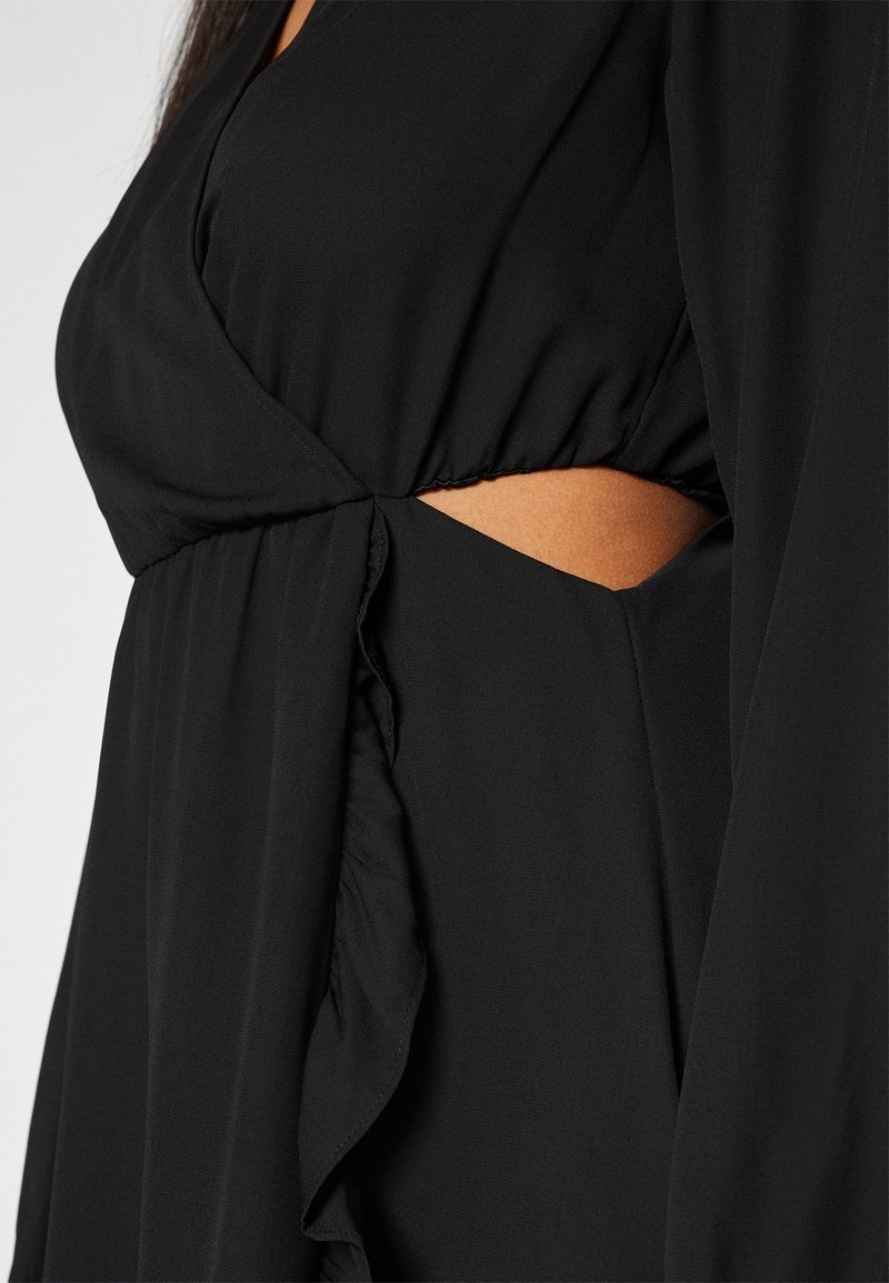 Abito nero con vita arricciata, maniche lunghe e un dettaglio cut-out sul lato. Il tessuto appare liscio e leggero.