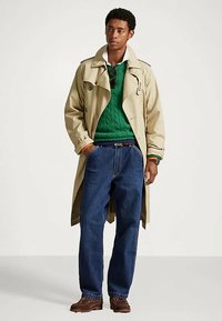 Beež trench coat, mille all on roheline soonikuga särk, sinised laiade jalgadega teksad ja pruunid kingad. Omab nuppe ja klassikalist kraed.