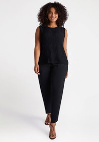 Top negro sin mangas con pliegues verticales, combinado con pantalones negros ajustados y tacones de tiras, que presenta un escote plano y una textura de tela suave.