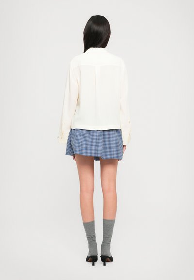 Kreemivärvi pikad varrukad särk, millel on vabalt langev lõige, koos sinise ruudulise mini seeliku, hallide põlvikute ja mustade kontsakingadega.