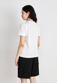 Tricou alb cu mânecă scurtă, cu guler rotund, purtat alături de șorturi cargo negre cu buzunare frontale. Material din bumbac neted, design simplu.