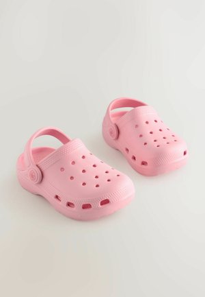 Růžové plastové nazouváky s kruhovými větracími otvory, zadním páskem pro pevné uchycení, texturovanou podrážkou a logem na boku.