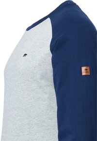 Graues und marineblaues Langarmshirt aus Baumwolle, mit Raglanärmeln, einem kleinen schwarzen Logo auf der Vorderseite und einem braunen Lederschild am Ärmel.