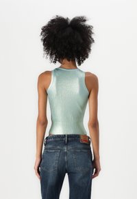 Top in tessuto metallico verde chiaro con texture a coste e design aderente, abbinato a jeans denim blu scuro con etichetta sul retro.
