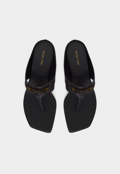 Ζευγάρι μαύρα σανδάλια με τετράγωνη μύτη και μεταλλικές χρυσές λεπτομέρειες, με επώνυμα πέλματα, σε λευκό φόντο.