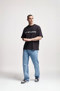 Black cotton T-shirt featuring "2Y STUDIOS" logo, paired with light blue denim jeans and black and white sneakers. Simple, casual fit.