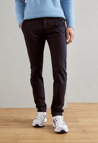 Chino neri con vestibilità affusolata, abbinati a sneakers bianche e viola. L'outfit include un maglione lavorato a maglia blu chiaro per creare contrasto.