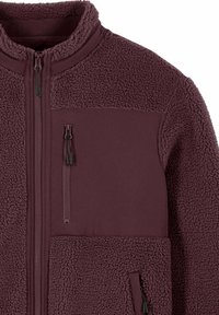 Veste polaire en bordeaux foncé, avec une partie supérieure texturée, un tissu inférieur lisse, des poches zippées et un col montant.