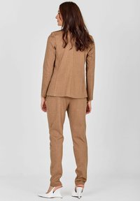 Pruun raitline ülikonnajakke ja pükse, millel on kohandatud sobivus ja sile tekstuur. Koos valgete kõrgete kontsadega.