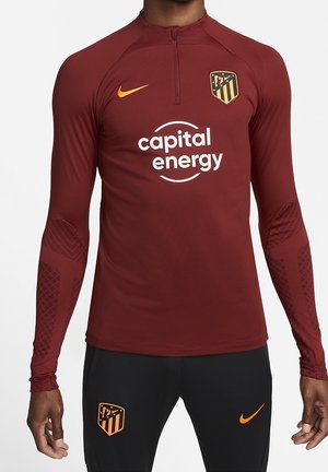 Haut de sport à manches longues bordeaux avec écusson Atlético Madrid, logo Nike et texte du sponsor "capital energy", porté avec un pantalon d'entraînement noir.