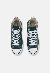 Zapatillas altas de lona verde oscuro con cordones blancos, puntera de goma y detalles de costura en contraste. Logo redondo clásico en el lateral.