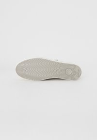 Valkoiset tennarit, joissa on kuvioitu kumipohja, jossa on aallokkokuva. Sivussa oleva etiketti lukee "Gabor". Siisti muotoilu ilman näkyvää metalliosaa.