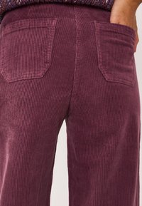 Corduroy broek in een diepe bordeauxkleur, met een verticale ribbelstructuur, twee achterzakken en een rechte pijp.