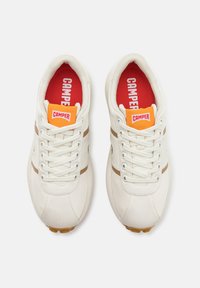 Vita atletiska skor med beige ränder, snörningsdesign och röda innersulor med "Camper"-logotypen. Mjukt material med en slät yta.