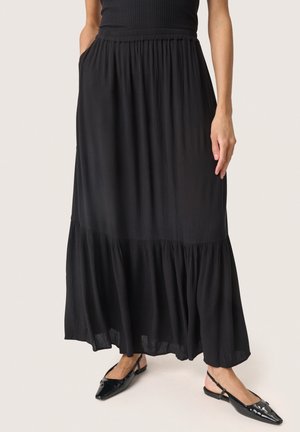 Schwarzer Maxirock mit einem gestuften Design, plissierter Textur und elastischem Bund. Getragen mit schwarzen Slingback-Ballerinas; verfügt über seitliche Taschen.