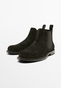 Un paio di stivali Chelsea in suede neri con pannelli laterali elastici e linguette, esposti su sfondo bianco.