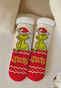 Calze pelose rosse e bianche con un Grinch verde che indossa un cappello da Babbo Natale rosso, con la scritta "Feelin' Grinchy" e motivi natalizi.