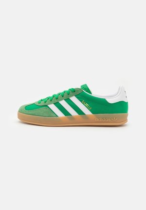 Basket Adidas Gazelle verte avec des bandes blanches, semelle en gomme et détails en daim, vue de côté sur fond uni.