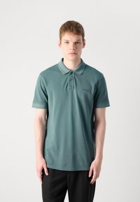 Grønn polo skjorte laget av mykt stoff, med en klassisk krage, to-knapps stolpe, og en subtil logo brodert på brystet.