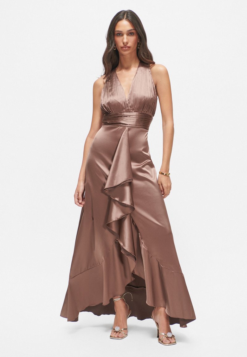 Langes braunes Satin-Kleid mit tiefem V-Ausschnitt, plissiertem Oberteil und asymmetrischem Rüschendetail, ergänzt durch sandfarbene, metallische High Heels.