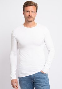 Witte lange mouwen shirt gemaakt van zacht, rekbaar materiaal. Heeft een ronde halslijn en een slim fit, in combinatie met blauwe spijkerbroek.